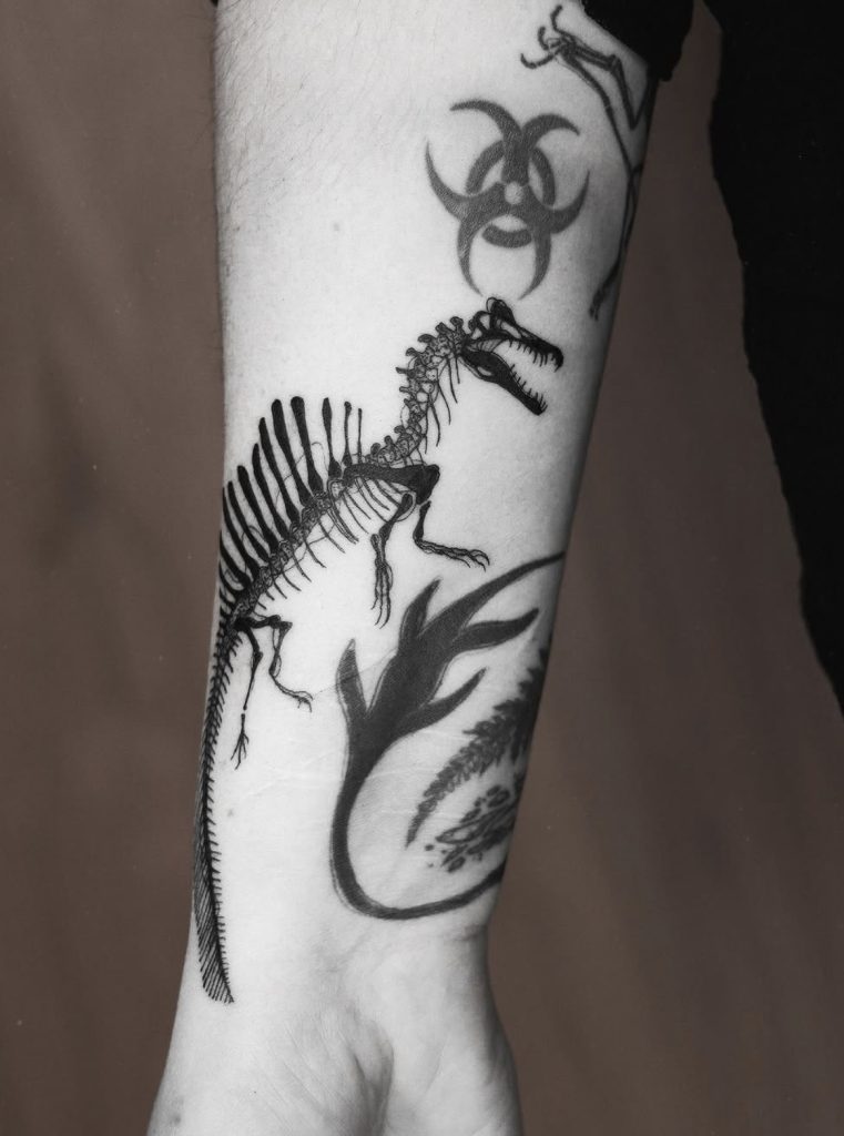 Blackwork-tattoo van een dinosaurusskelet op de onderarm, door Mara.