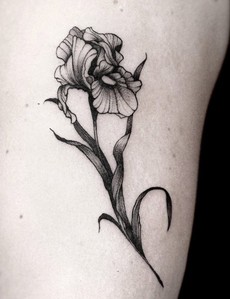 Zwarte bloem-tattoo met sierlijke bladeren en fijne lijnen, door Sonja.