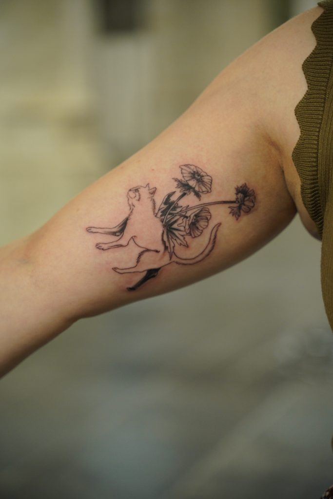 Kattentattoo met bloemen op Chava’s arm, gezet door Roger.