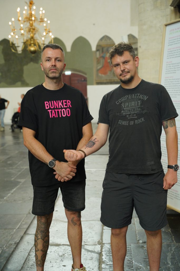 Robert showing his shield tattoo alongside tattoo artist Mitchel
