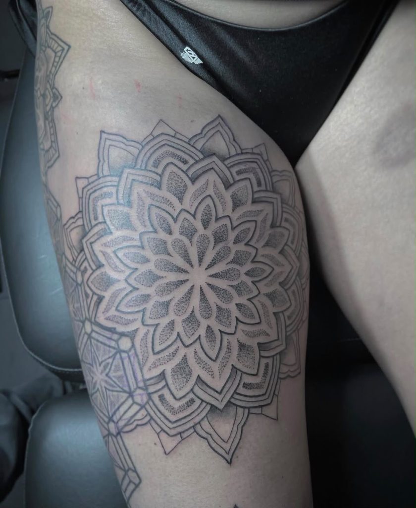 Mandala tattoo met gelaagde bloemvormen, fijne lijnen en stippen op een bovenbeen, door Kenneth.