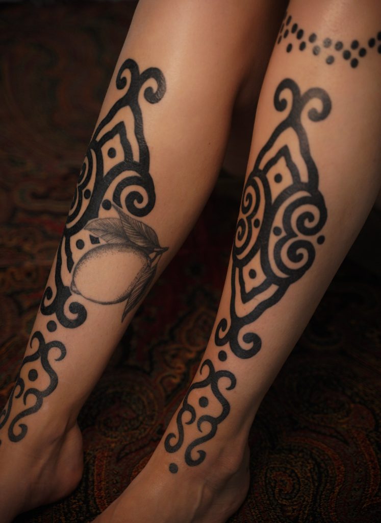 Zwarte ornamentale tattoos met brede krullen en stippen op beide onderarmen, door Roos.