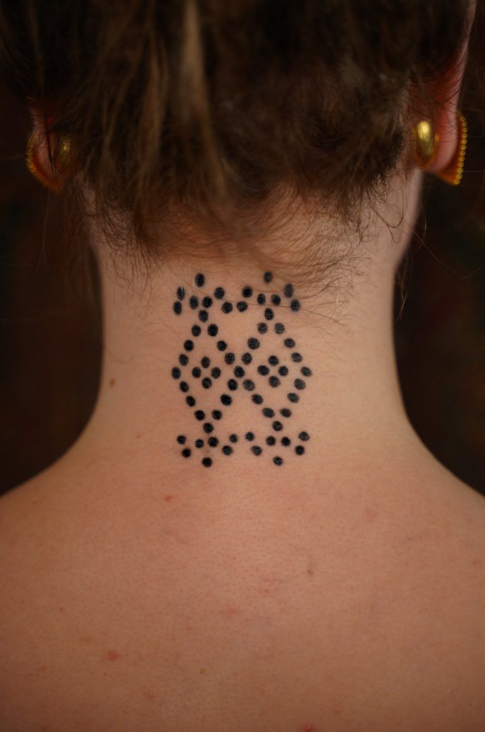 Symmetrische ornamentale tattoo van zwarte stippen midden in de nek, door Roos.