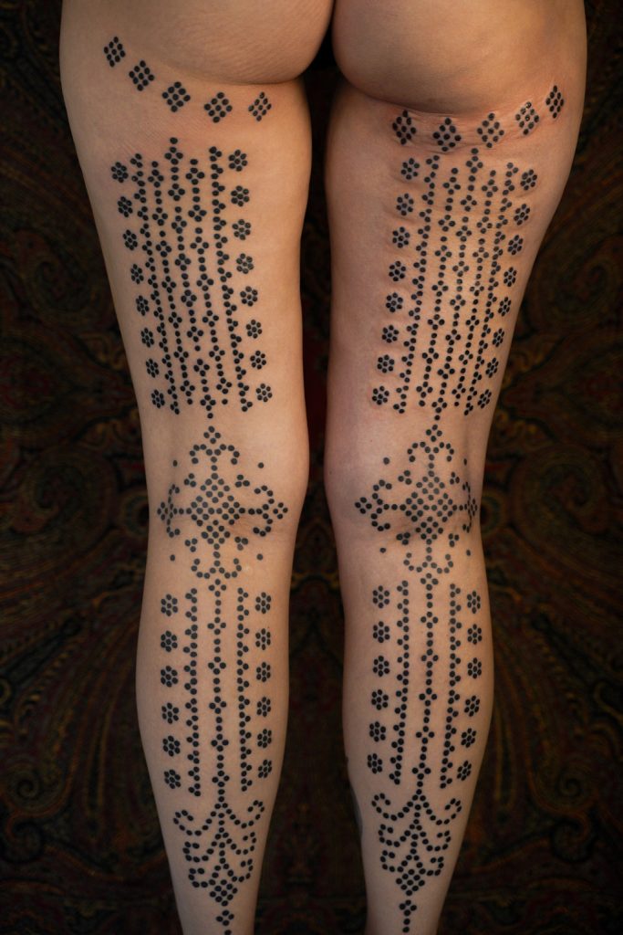 Symmetrische ornamentale tattoos met zwarte stippen op beide benen, door Roos.