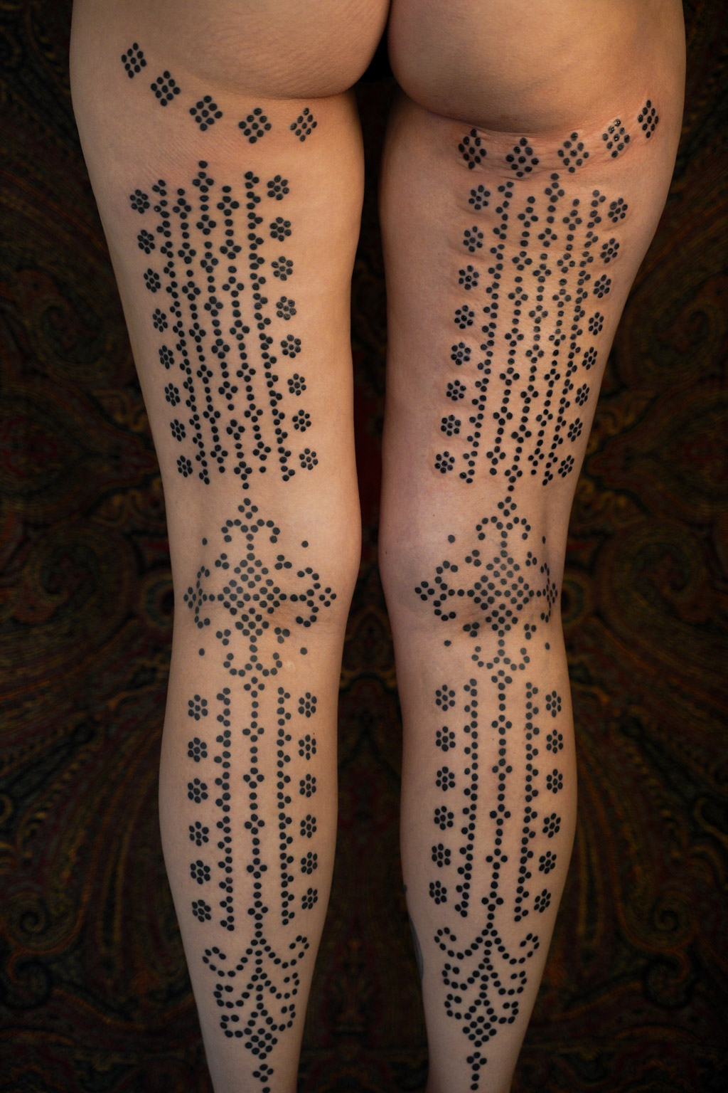 Symmetrische ornamentale tattoos met zwarte stippen op beide benen, door Roos.