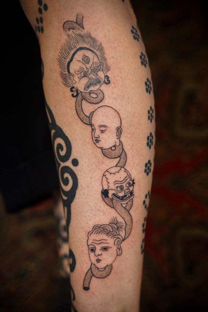 Blackwork tattoo van vier gezichten verbonden door linten op een been, door Roos.