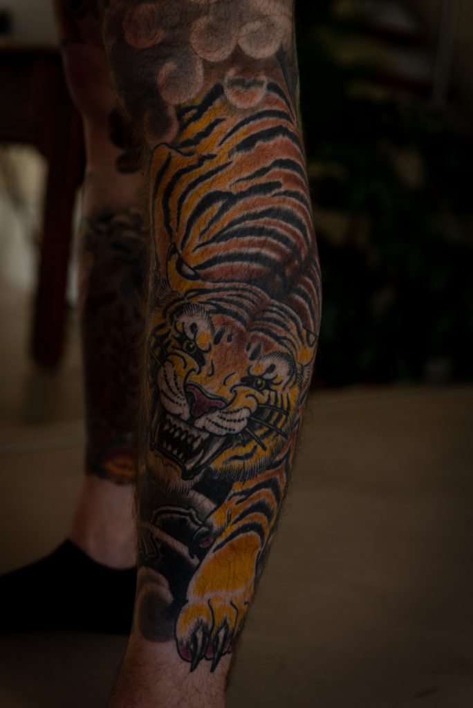 A tiger tattoo on Erik’s leg, with black stripes and warm orange tones.