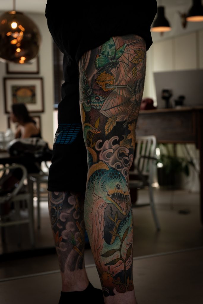 A green fantasy creature, butterflies and leaves in Erik’s leg tattoo.