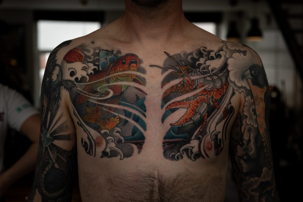 Erik’s chest tattoo with colourful fish, a lobster and waves.