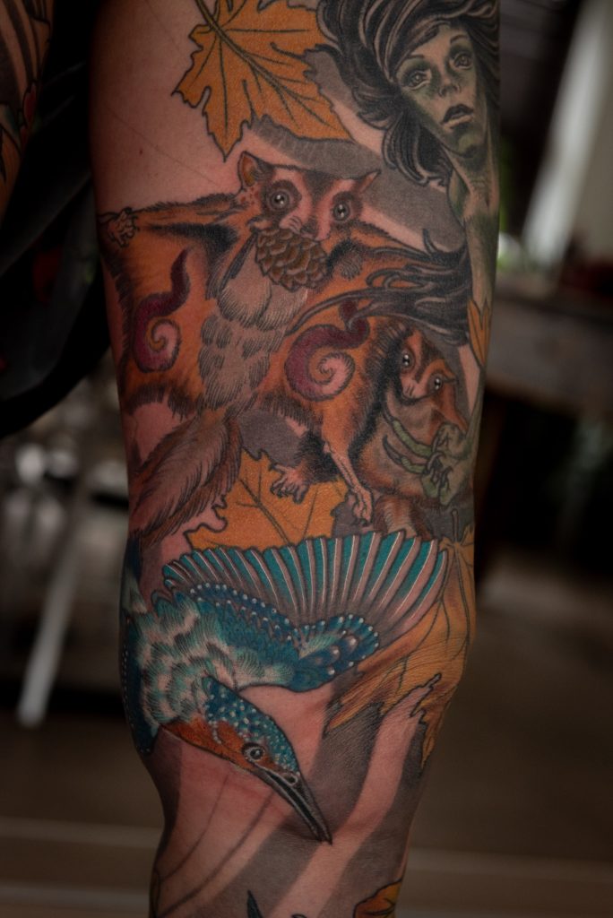 Detail of Lucie’s leg tattoo with a kingfisher, fantasy animals and a mermaid.